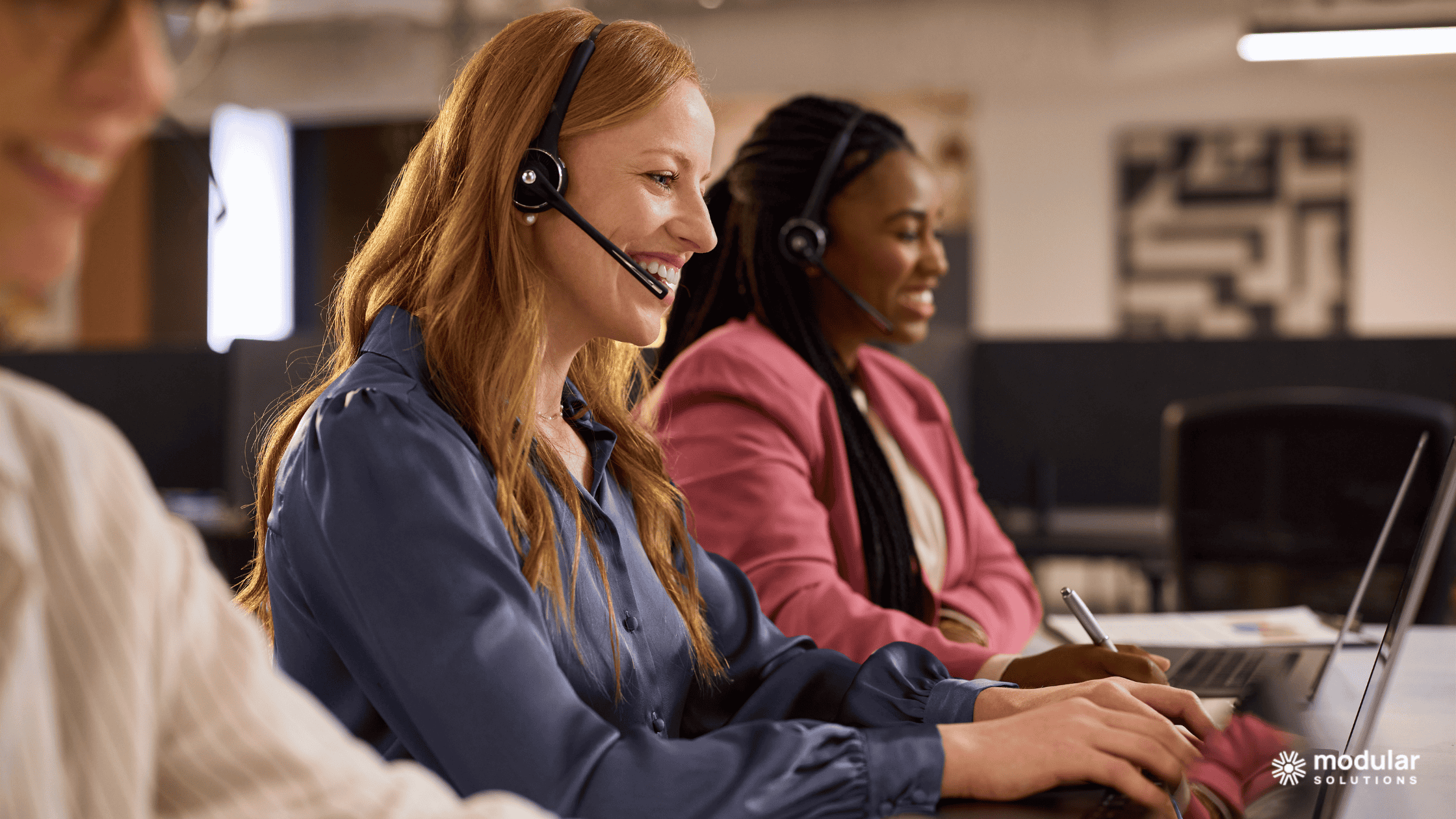 Three insurance brokers working on desktop computers (via broker portal) and wearing headsets. They're all looking pleased.