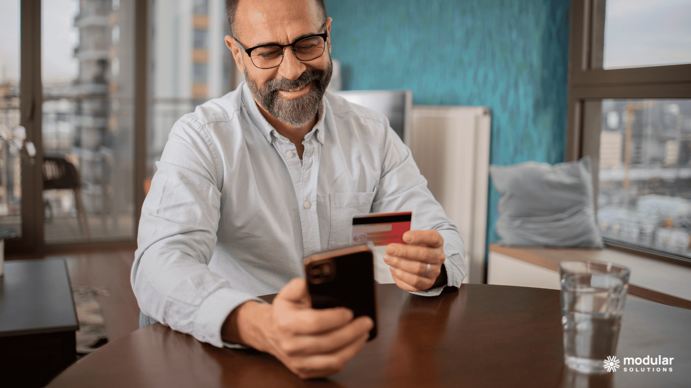 A middle-aged smiling as he holds a credit card and scrolls on his phone. He's using a direct-to-consumer insurance channel to buy insurance.