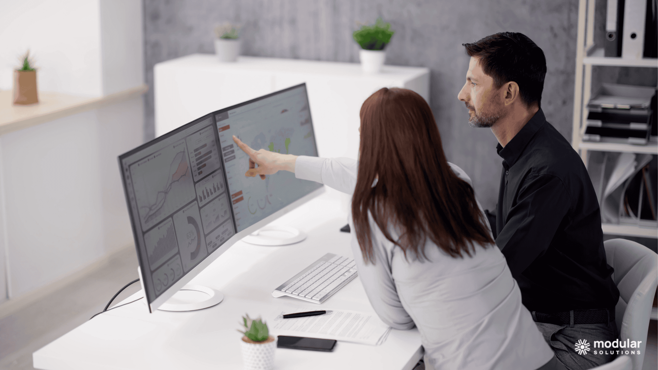 Two insurance employees reviewing data and analytics on two computer screens.